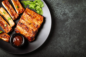 Hot grilled spare ribs from a summer BBQ served on a plate with sauce. Top view, a Food & Drink Photo by Budarinphoto