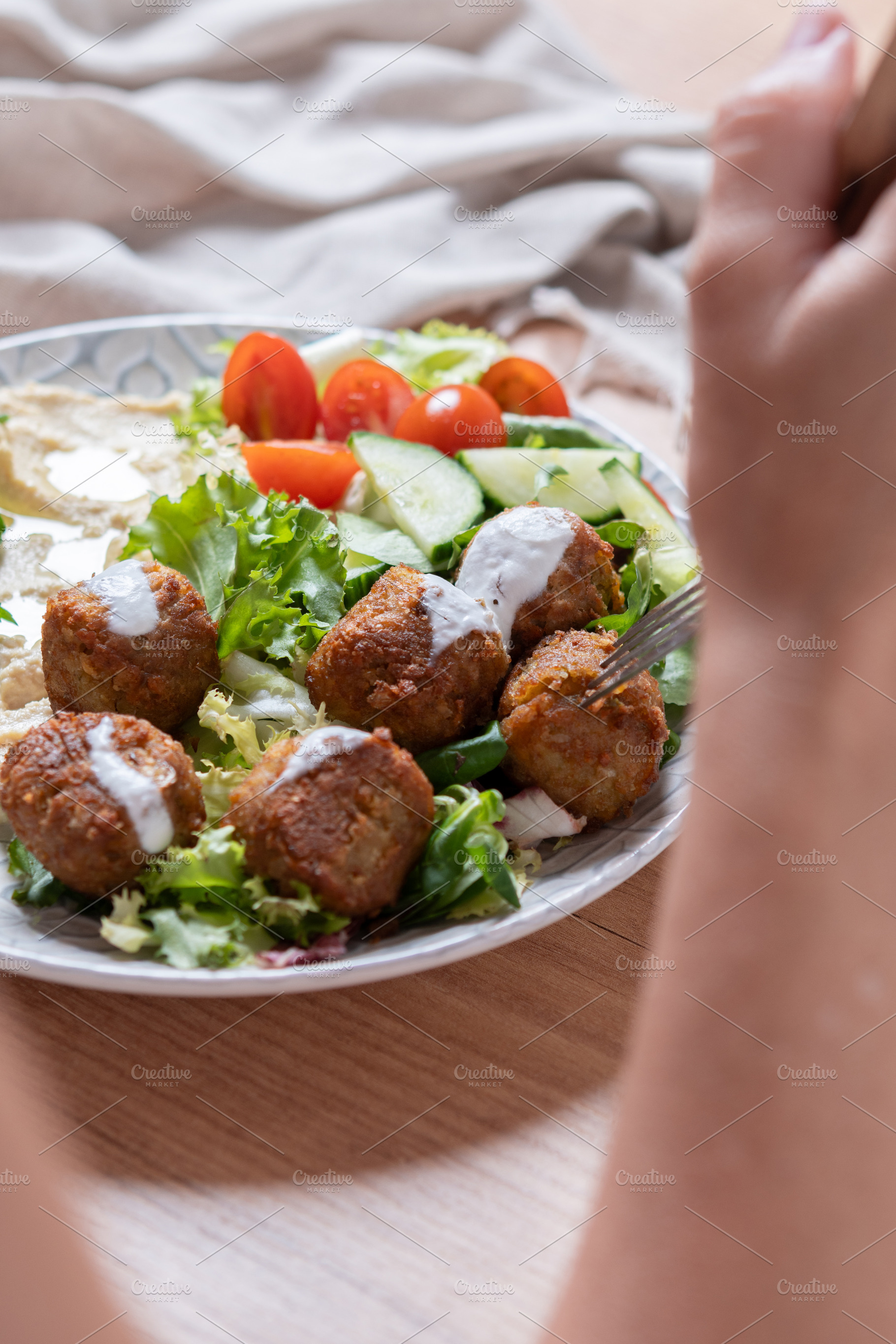 Person holding plate of falafel with hummus and fresh salad, a Food & Drink Photo by etorres69