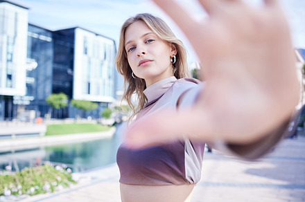 Portrait of woman in the city with hand reaching, standing in the street. Fashion, beauty and makeup in trendy young girl in the road of urban town with hand out to frame style model face in summer, a Photo by Peopleimages.com