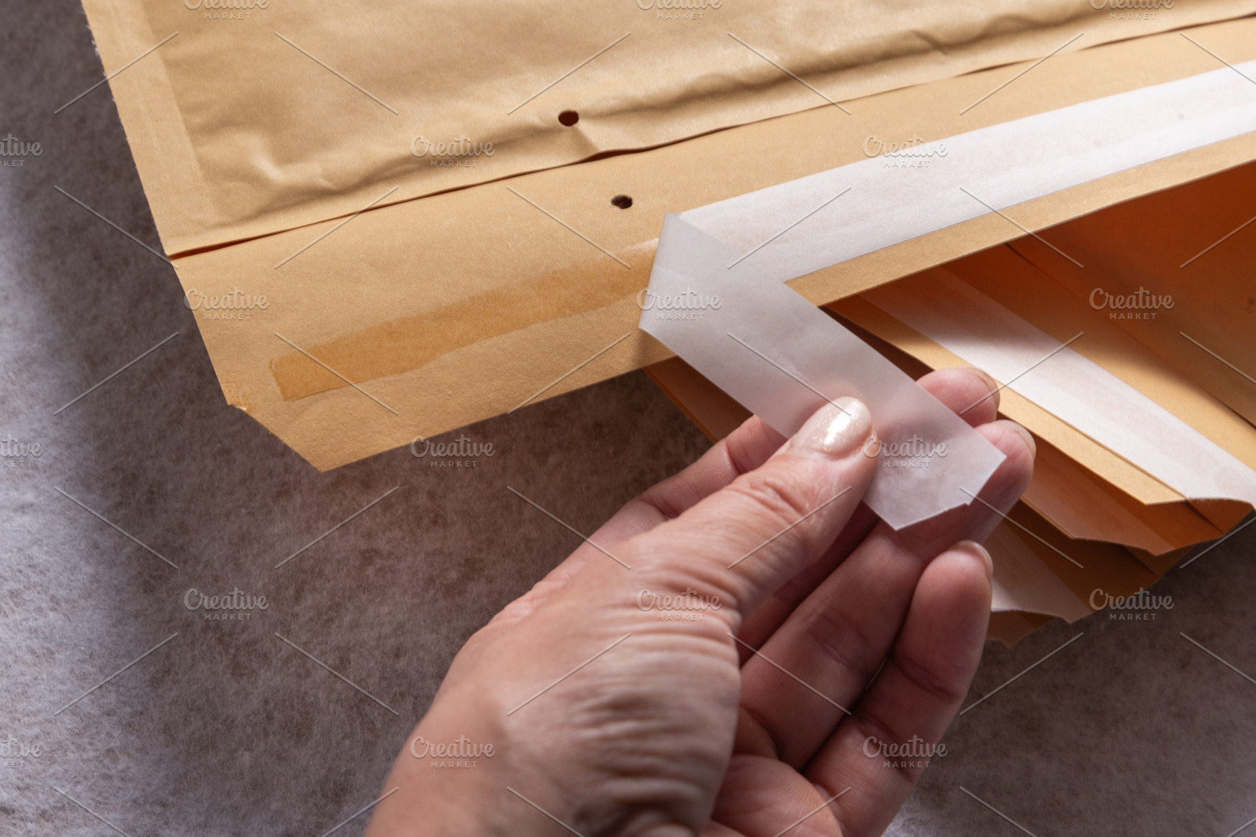 Female Hand Peeling Adhesive Tape on Bubble Mailer Plastic Padde, an Industrial Photo by MDBildes