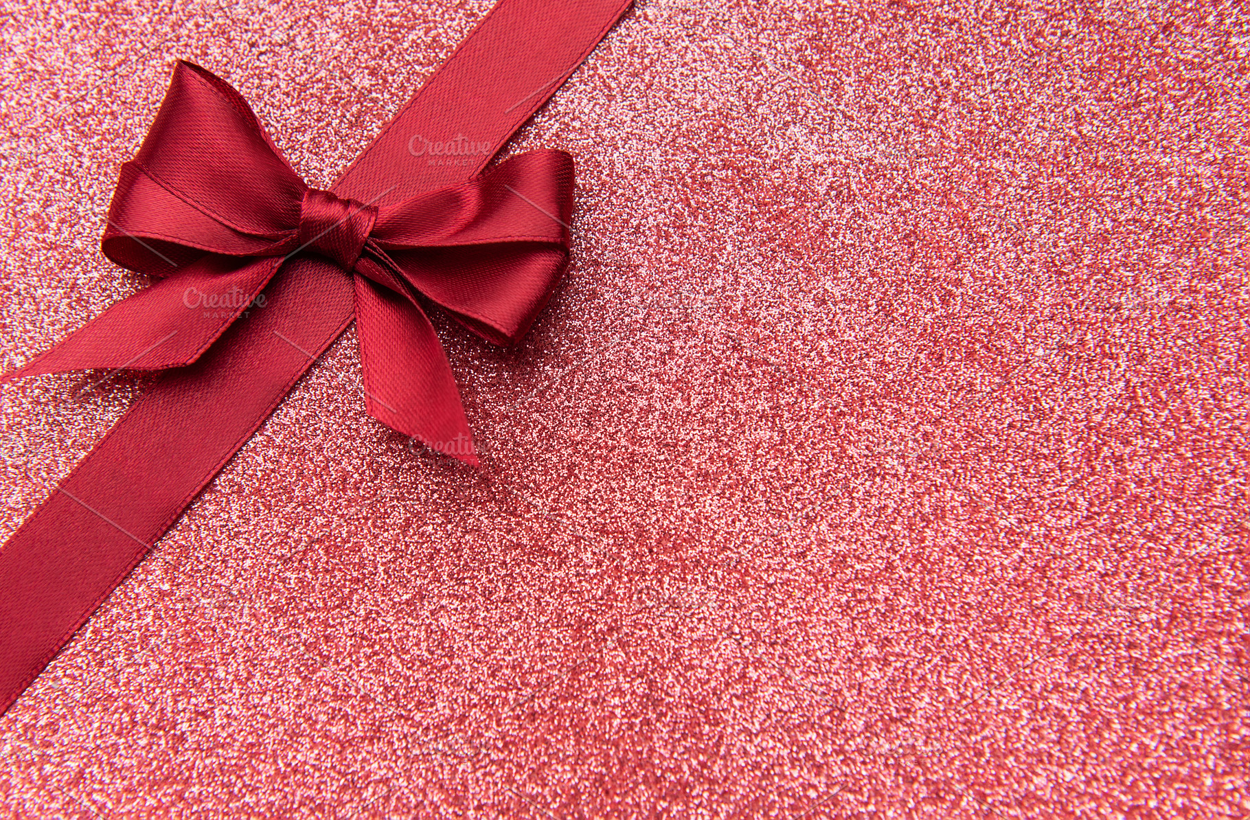 Red satin ribbon bow on sparkling glitter background, a Photo by Olena Rudo