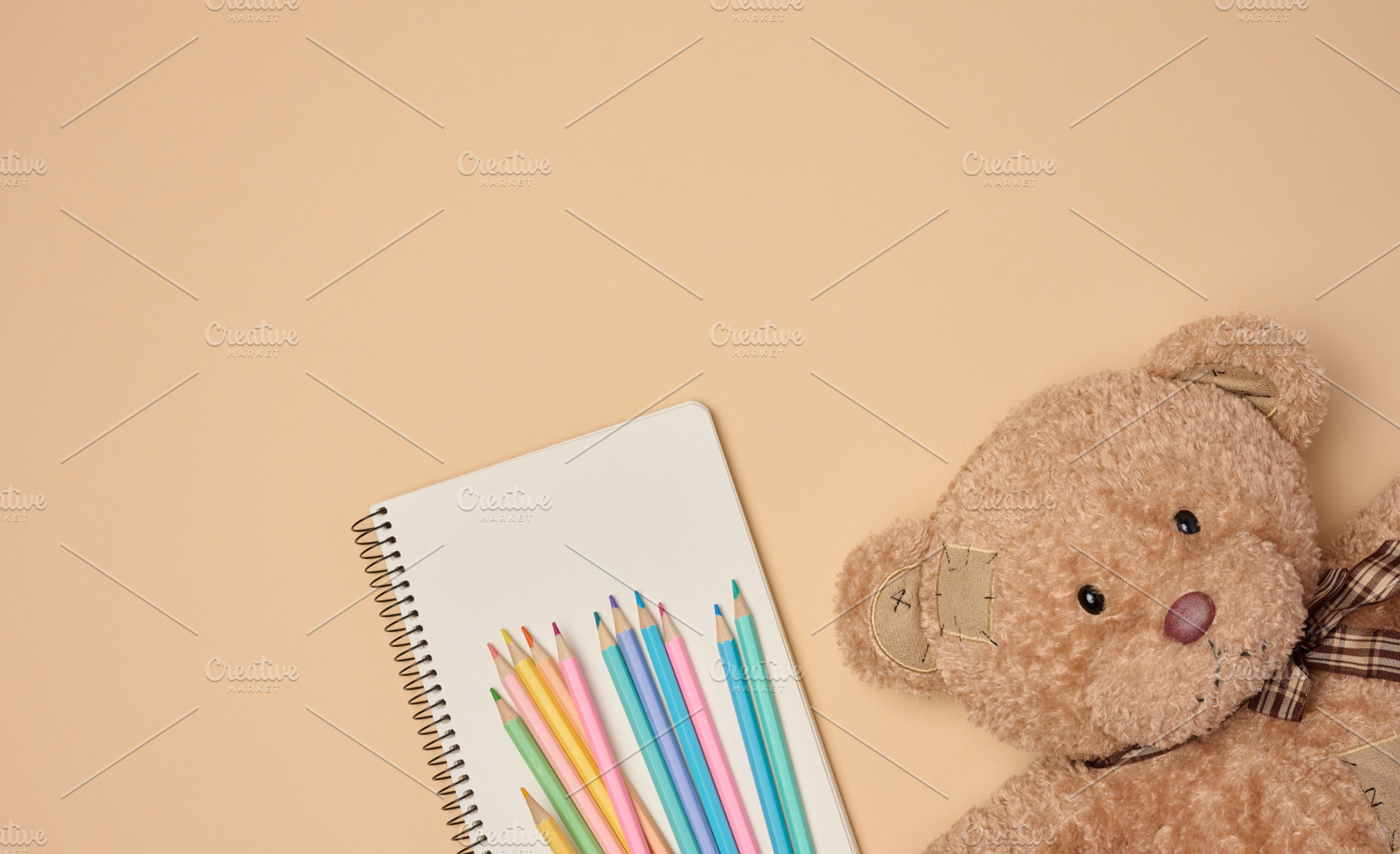 Wooden colored pencils and open notebook, brown teddy bear next, a School & Education Photo by ndanko