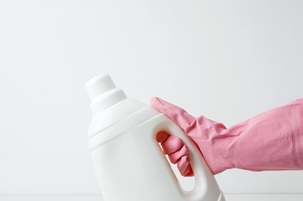 Female hand in a pink rubber glove holding a white branding mockup of laundry g