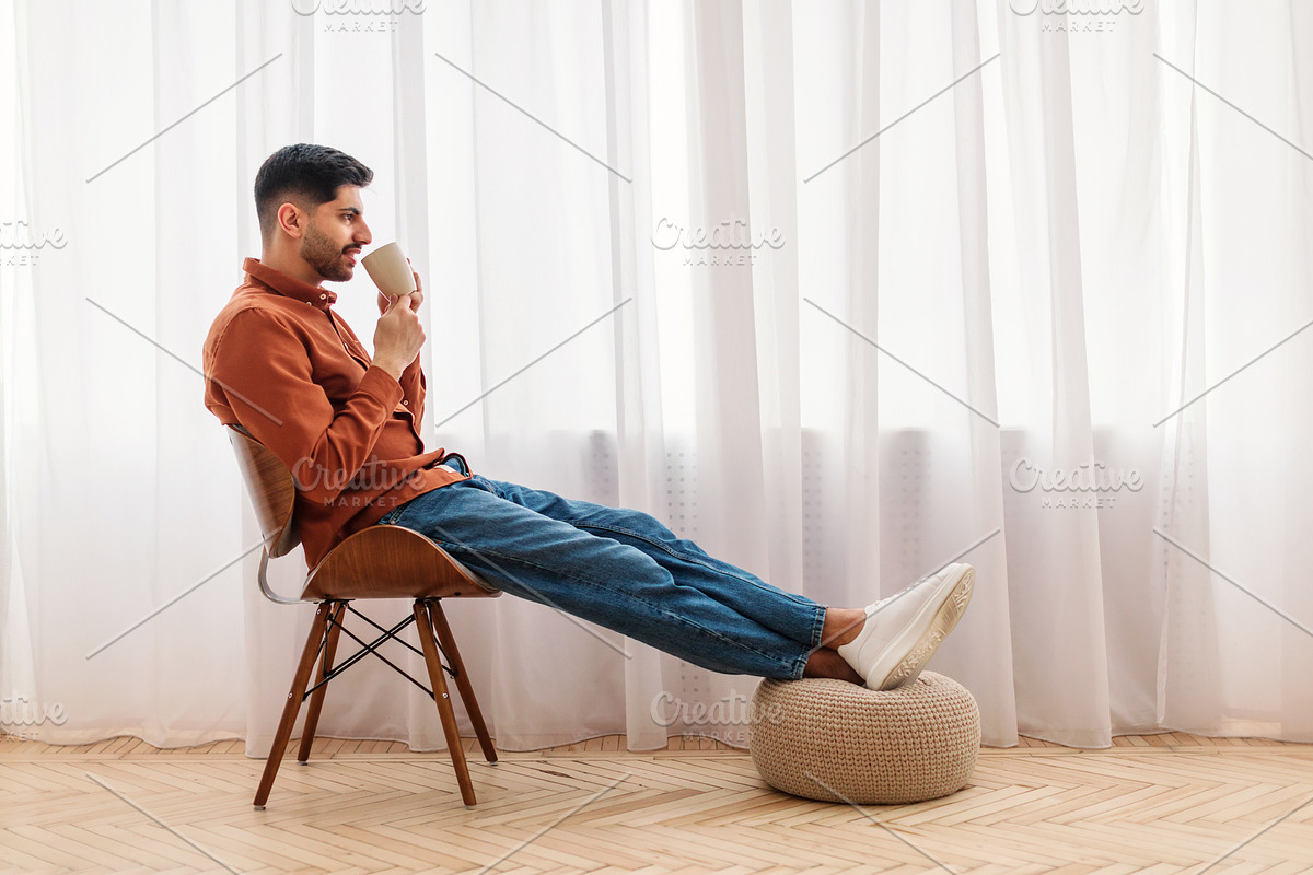 Man having rest at home sitting on chair, drinking coffee, a Photo by Prostock-Studio (Photo 1 of 2)