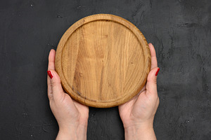 Female hand holding round wooden blank board on black background, a Food & Drink Photo by ndanko