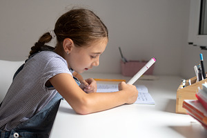 Smiling schoolgirl reading a notebook while studying at home, a Person Photo by etorres69
