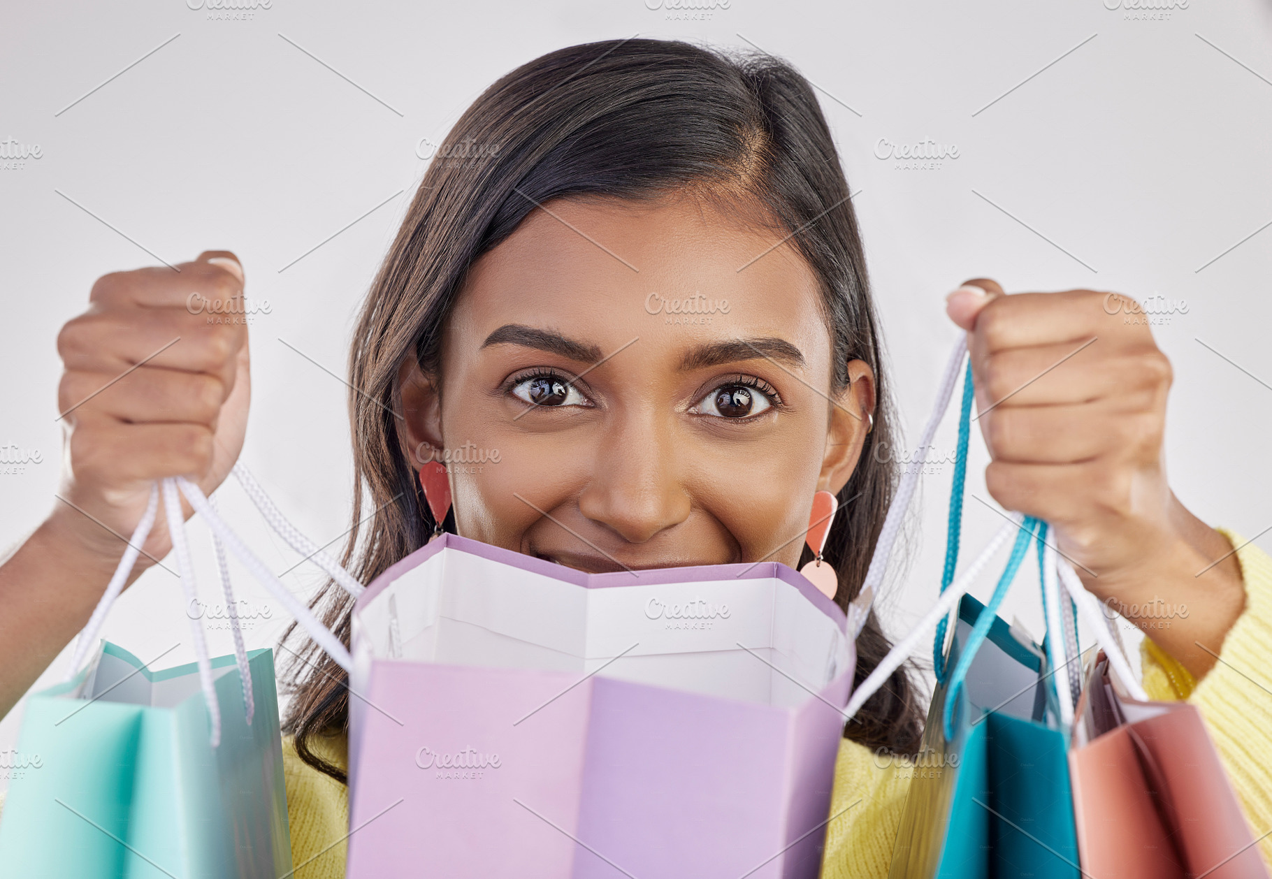 Portrait, shopping and eyes with a woman customer in studio on a gray background for retail or consumerism.  Fashion, luxury and excitement with a female consumer or shopper showing bags of bargains, a Photo by Peopleimages.com