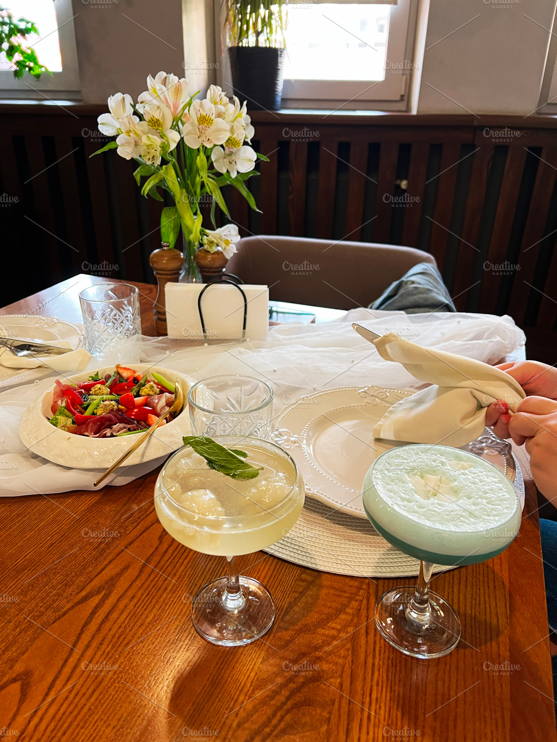 Elegant table setting with drinks, fresh salad, and white flowers centerpiece, a Photo by AS photostudio