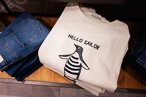 Folded white sweater with penguin design and text alongside blue denim jeans, a Photo by AS photostudio