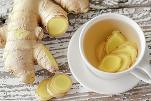 Cup of ginger tea with sliced ginger root on wooden table, a Food & Drink Photo by AlyaAnd