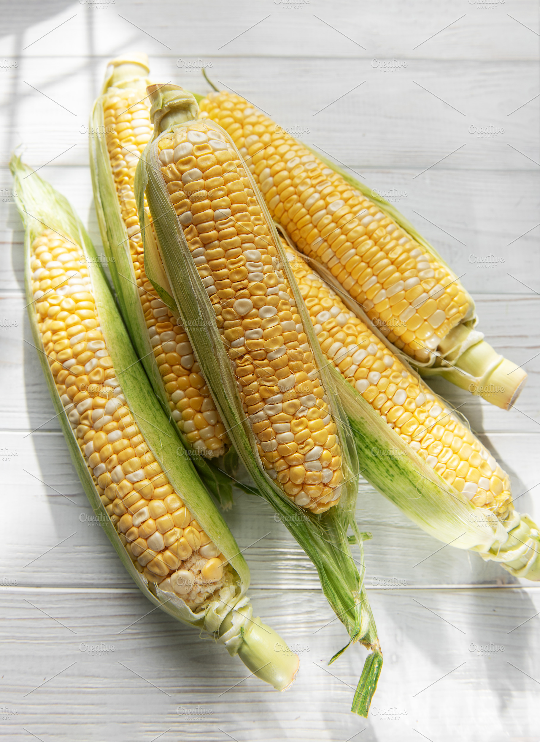 Fresh sweet corn cobs on white wood background, a Food & Drink Photo by Olena Rudo