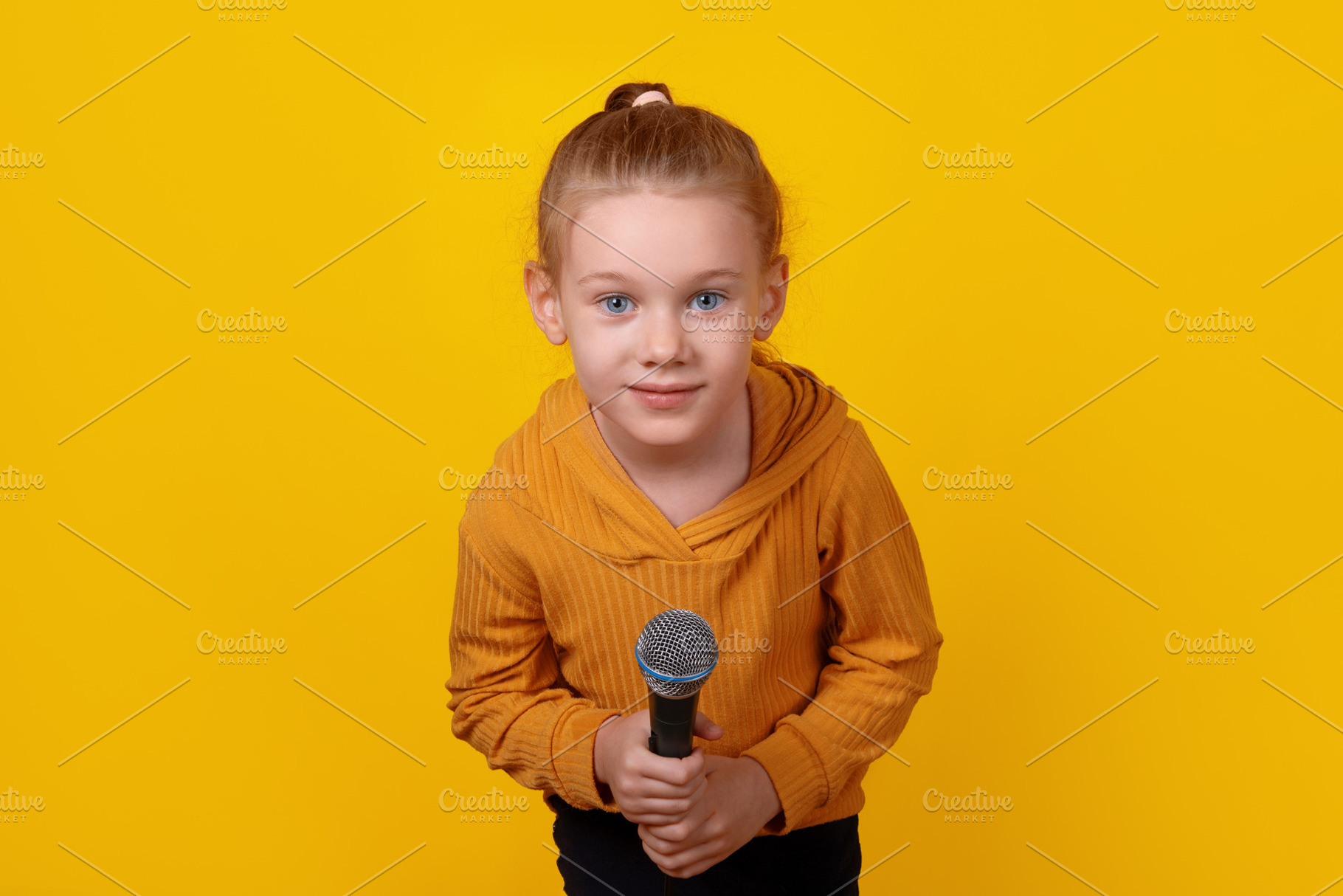 Smiling young girl in yellow hoodie holding a microphone against, a Person Photo by Ales Munt
