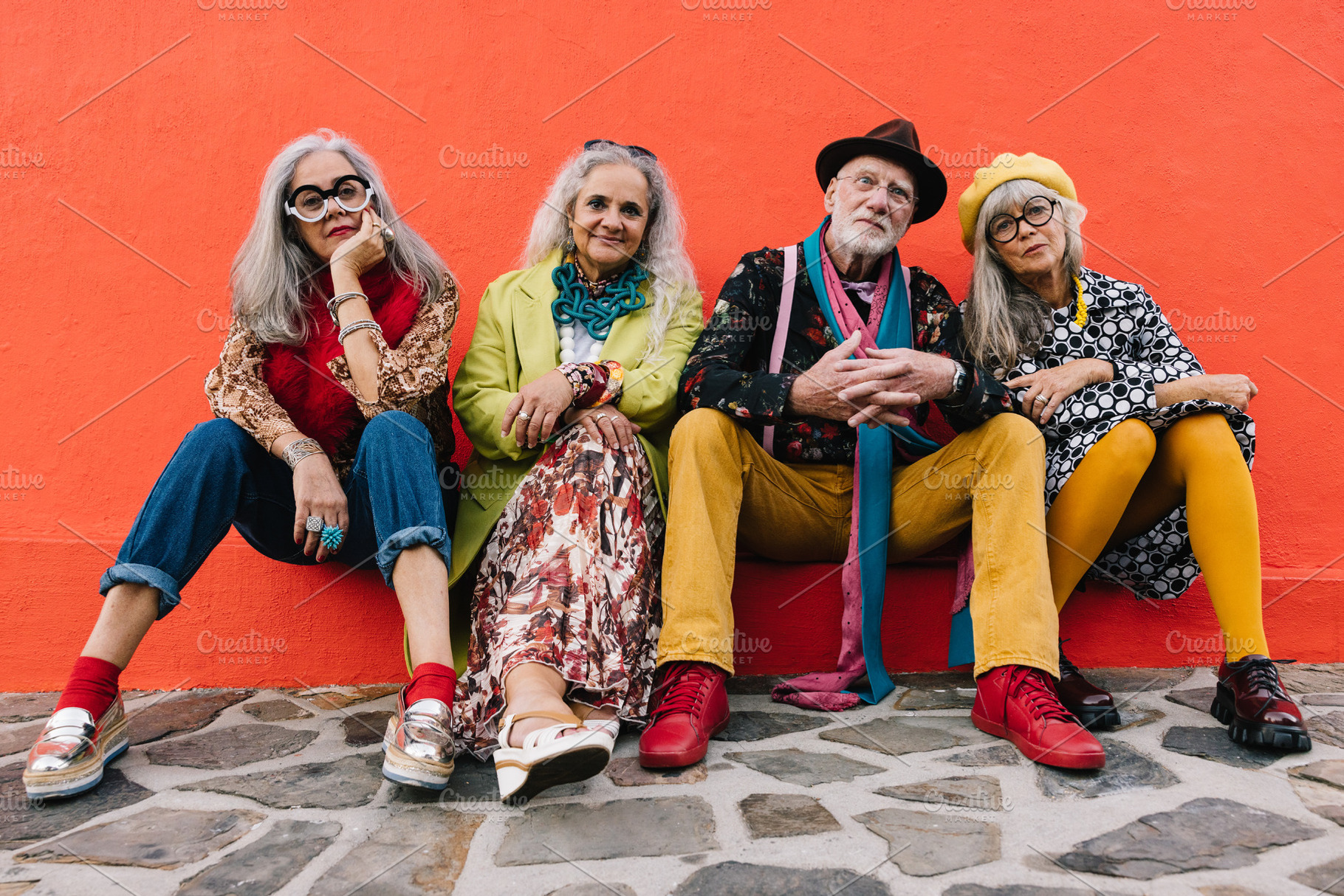Carefree elderly friends sitting against a red wall, a Person Photo by Jacob Lund