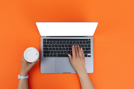 Female hands with paper cup on laptop on orange background, a Business Photo by AtlasStudio