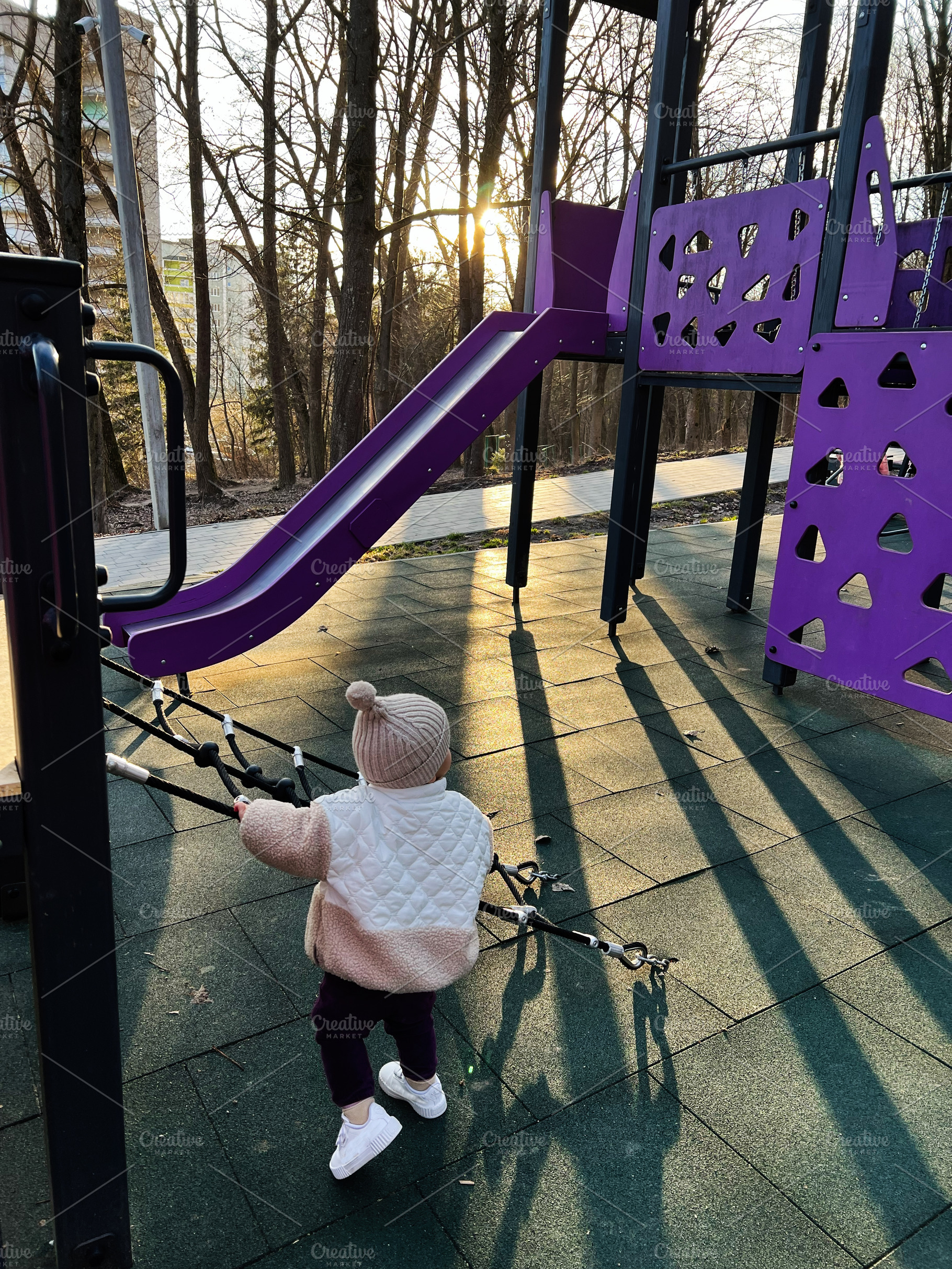 Child playing on a purple playground at sunset surrounded by trees, a Photo by AS photostudio