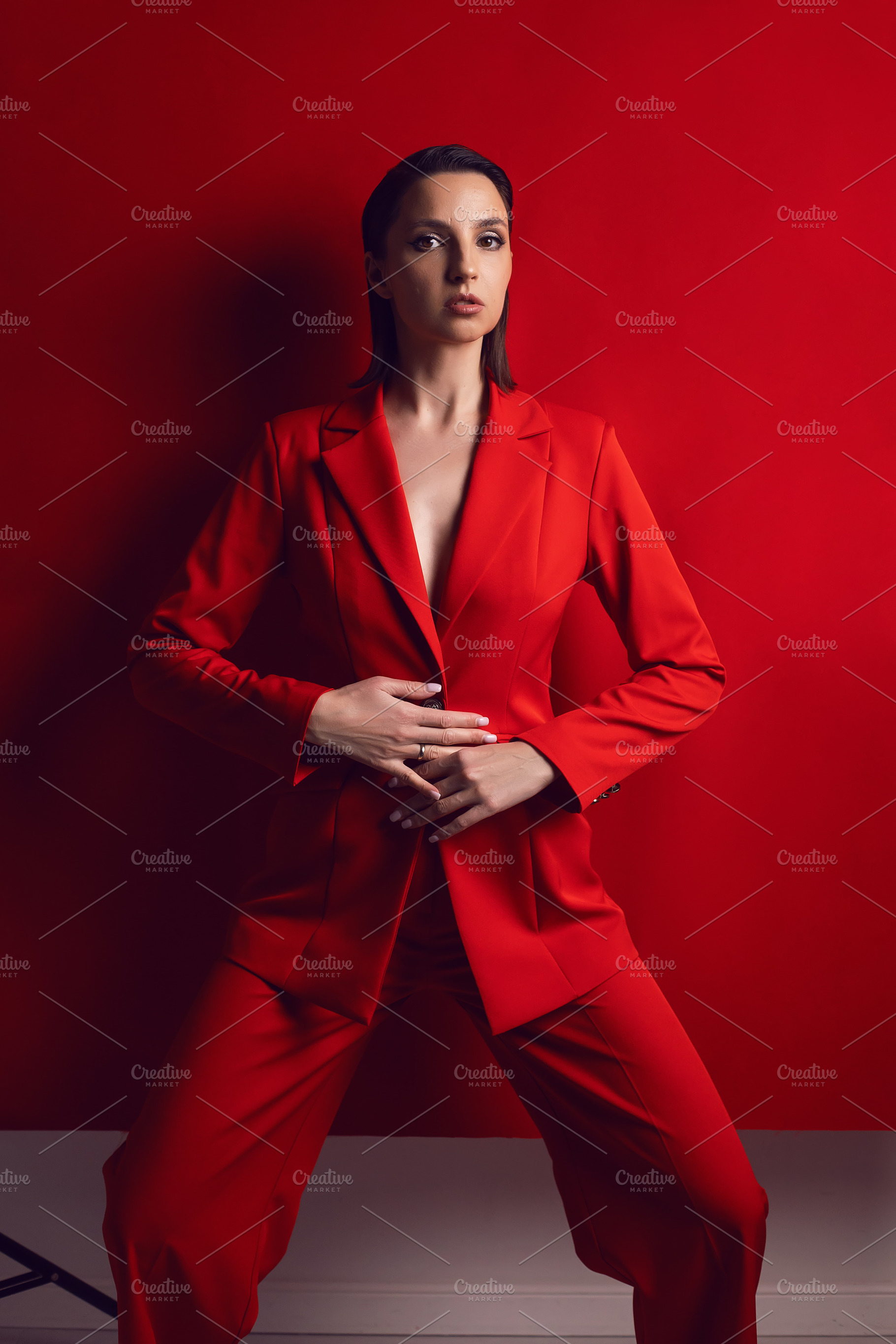 portrait of an elegant sexy woman in a red jacket and pants stands against the, a Person Photo by SaulichPhoto