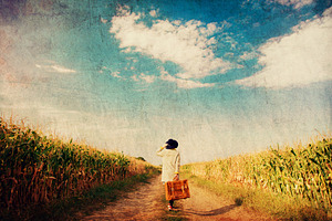girl coat with suitcase on a rural road near cornfield