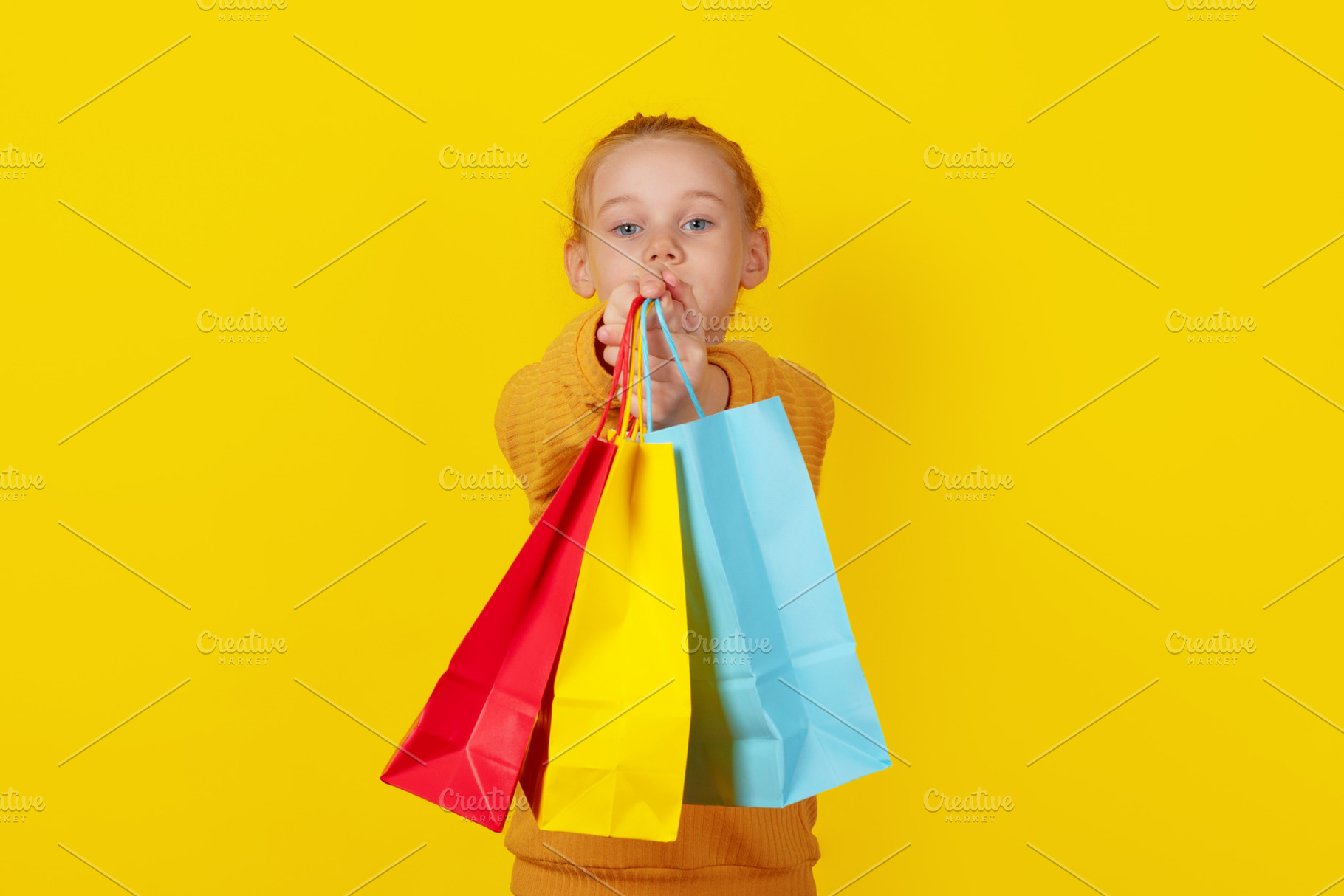 Smiling young girl holding colorful shopping bags on vibrant yel, a Person Photo by Ales Munt