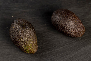 several whole black avocado fruits of small size on a black slate, a Photo by rsoollAI