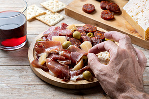 Hand picking up serrano ham from Spanish charcuterie board, a Food & Drink Photo by etorres69