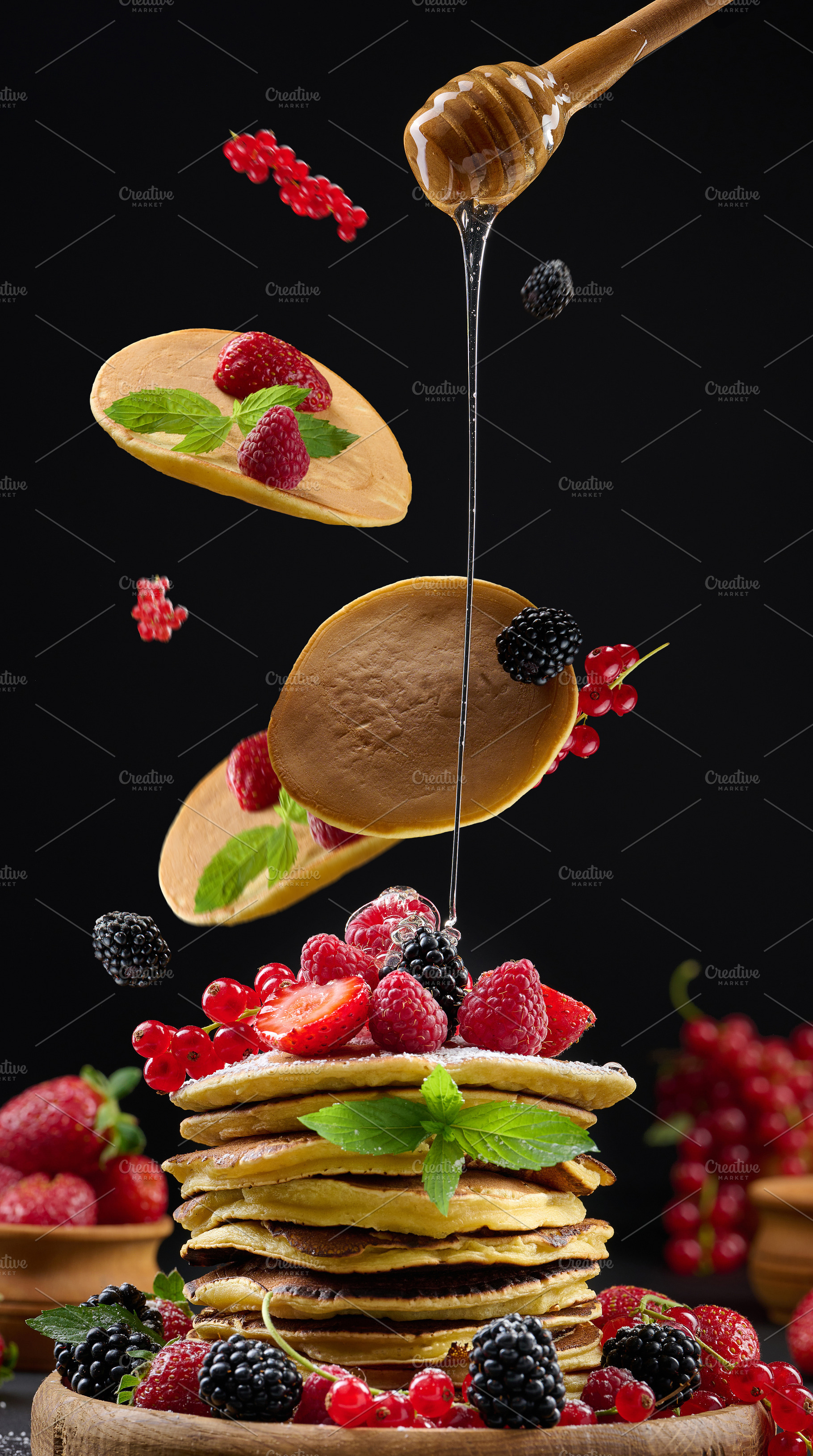 Pancakes fall on a stack of fritters with berries and mint, driz, a Food & Drink Photo by ndanko