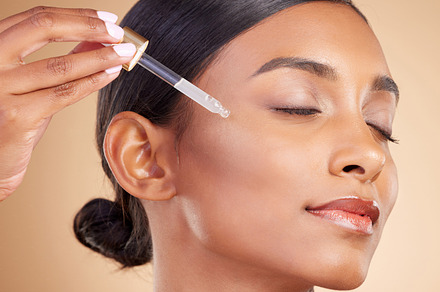 Woman, dropper and retinol on face for skincare beauty or cosmetics against studio background. Calm beautiful female model applying oil drop to skin for hydration, moisturizer or facial treatment, a Photo by Peopleimages.com