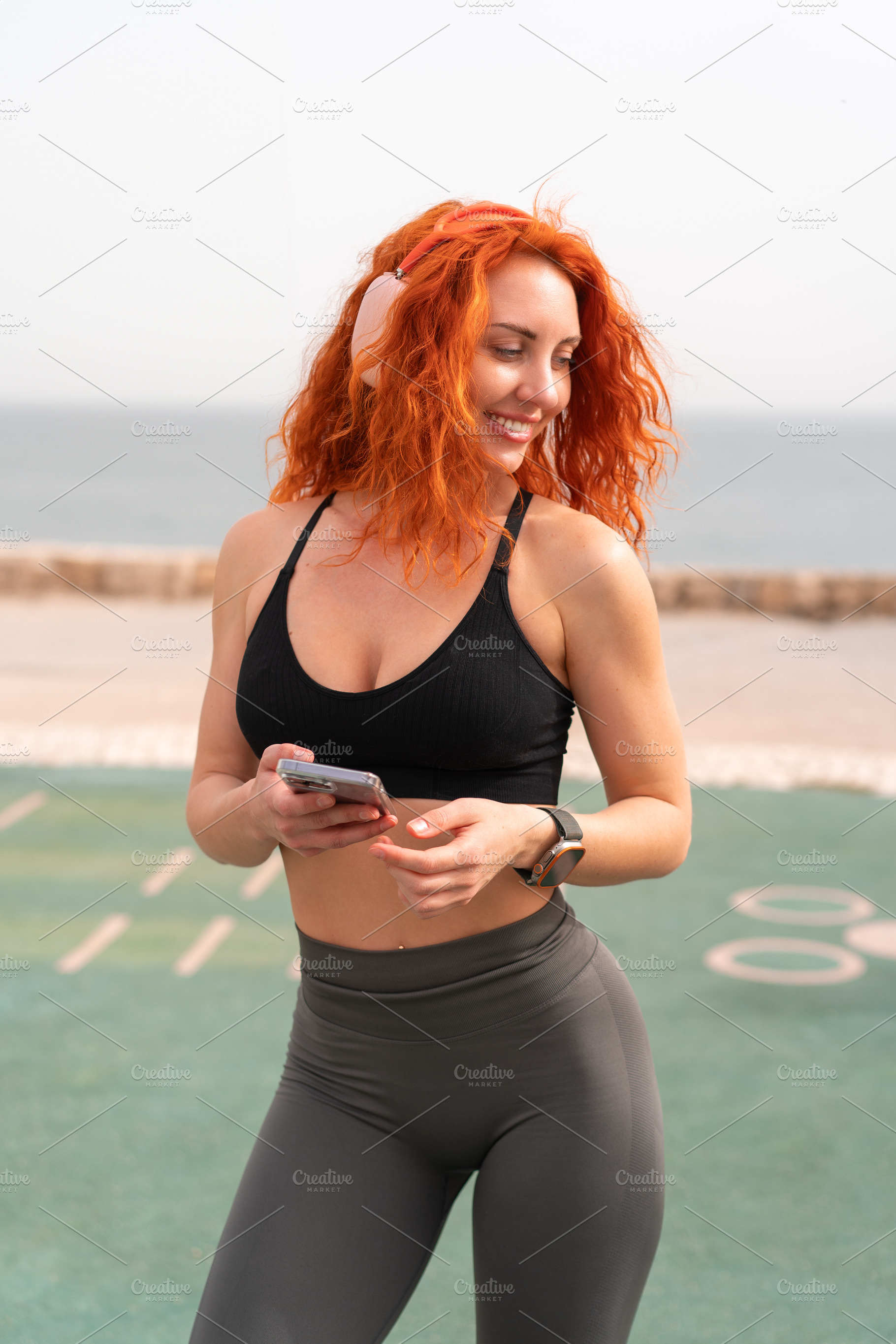 Happy sporty woman holding smartphone while standing at outdoor gym, a Person Photo by andreonegin market