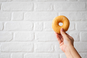 Hand Holding Glazed Donut with Copy Space on White Brick Background, a Food & Drink Photo by etorres69