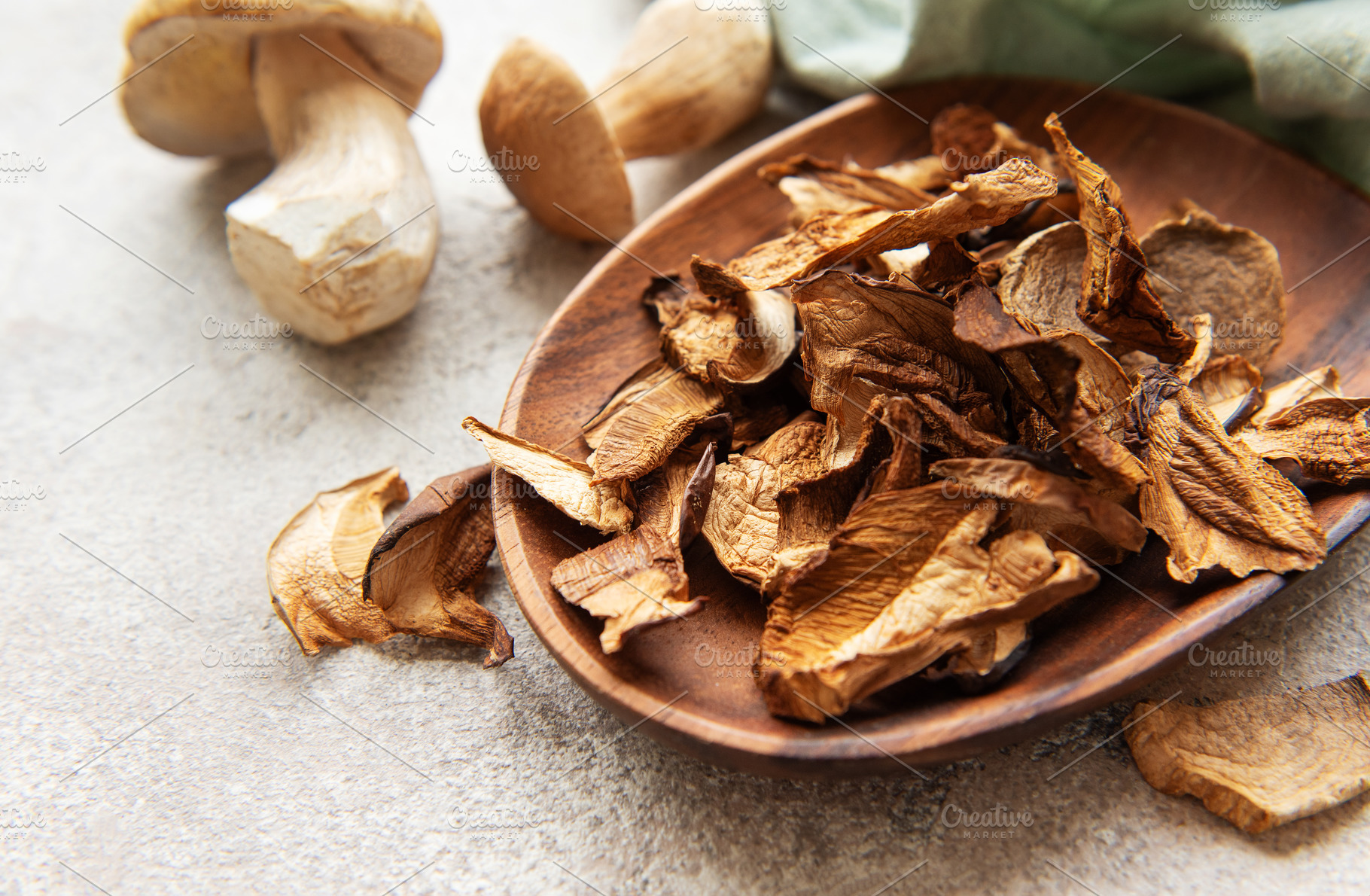 Dried porcini mushrooms resting in wooden bowl on gray textured, a Food & Drink Photo by Olena Rudo