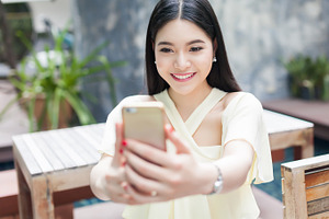 Asian woman taking a selfie with her phone in public park focus on her face