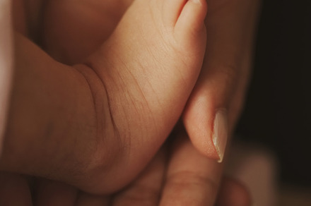 Mother holds little foot of newborn baby containing baby, mother, and feet