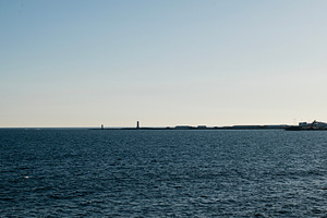 Coastal view of Akranes harbor with lighthouses and calm ocean under clear sky, a Photo by AS photostudio