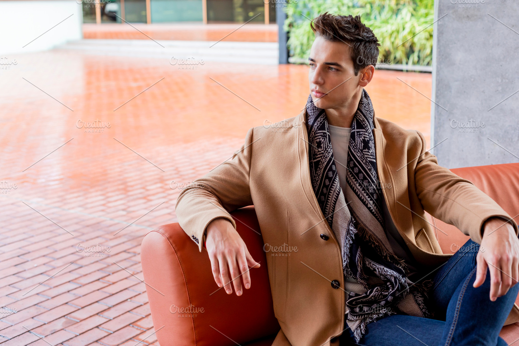 Stylish man seated on sofa in modern urban setting, a Person Photo by RF Images