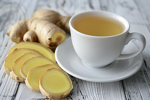 Cup of ginger tea with sliced ginger root on wooden table, a Food & Drink Photo by AlyaAnd
