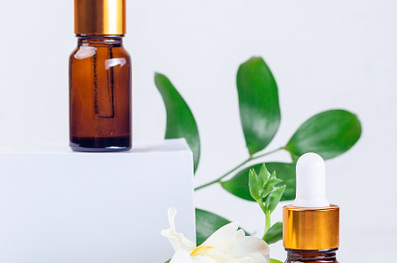 Brown glass pipette bottles with white podium, flowers and green leaves, vertic, a Beauty & Fashion Photo by iuliia_n