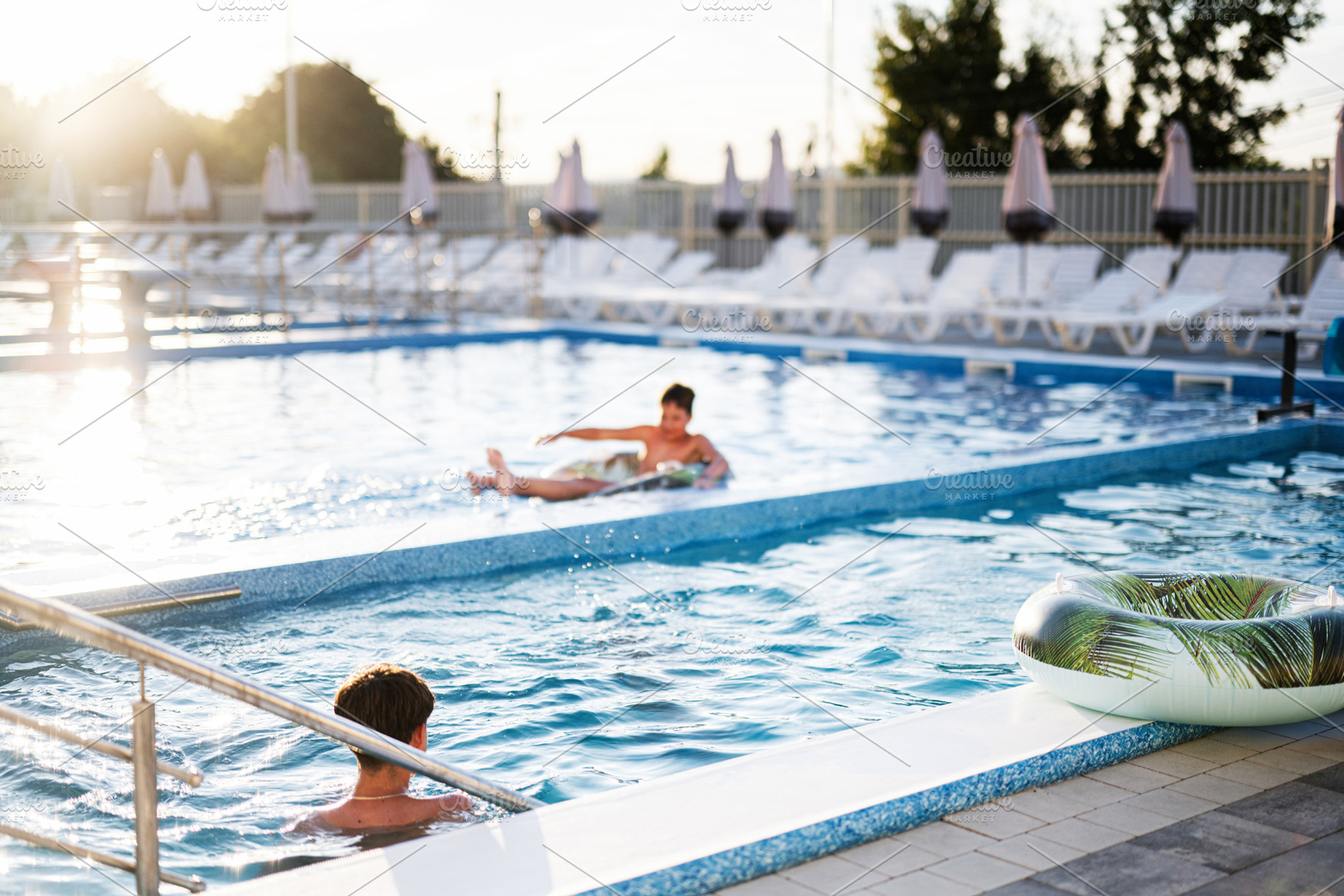 Children playing and relaxing in an outdoor swimming pool at sunset, a Photo by AS photostudio