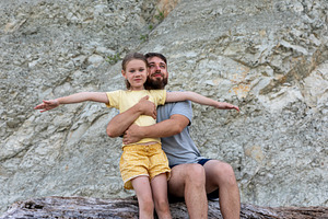 Father embraces his smiling daughter on a rocky backdrop, both looking joyful a, a Person Photo by Ales Munt