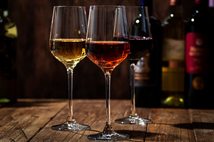Red, white and rose wine in glasses on wooden background and col
