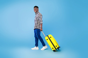 Happy young African American man walking with bright suitcase, going on summer, a Photo by Prostock-Studio