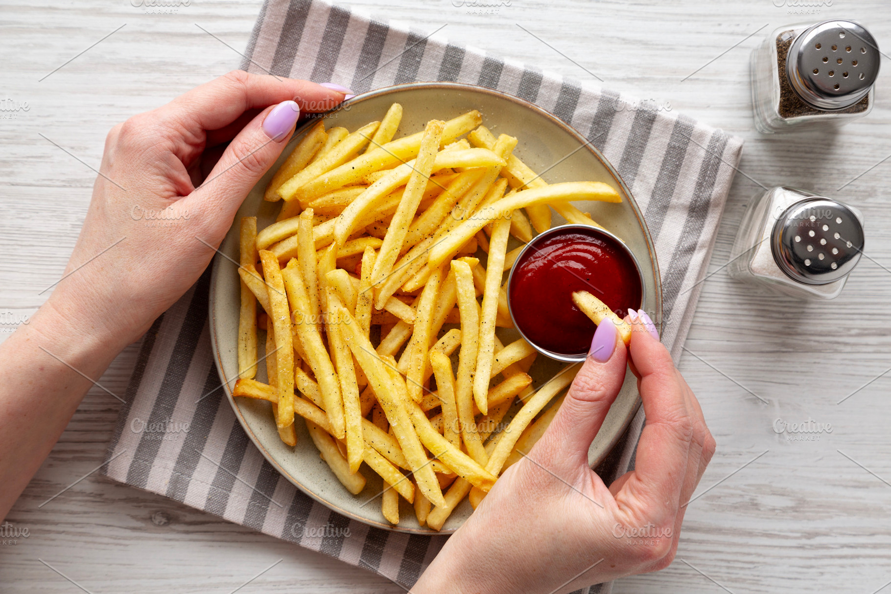 Woman dipping French Fries into Ketchup, overhead view., a Food & Drink Photo by LiudmylaChuhunova