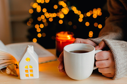 Cozy winter still life. Women holding a mug with tea or coffee, burning candle,