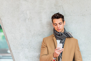 Stylish man texting on smartphone against concrete wall, a Person Photo by RF Images