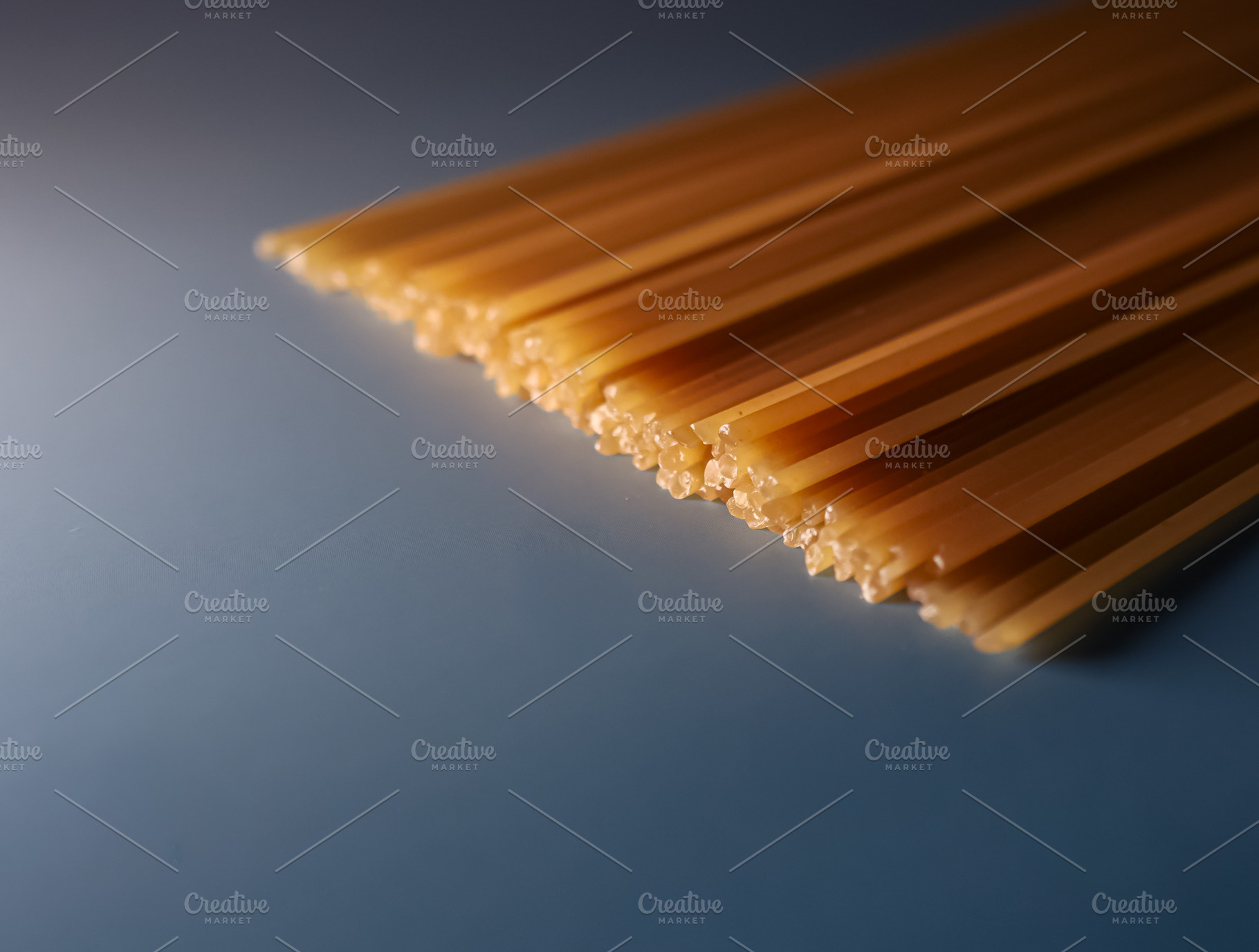 Dry spaghetti pasta strands forming abstract pattern on blue background for Ita, a Photo by Studio ANNA