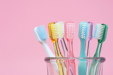 New toothbrushes in glass on pink background, a Health & Medical Photo by AlyaAnd