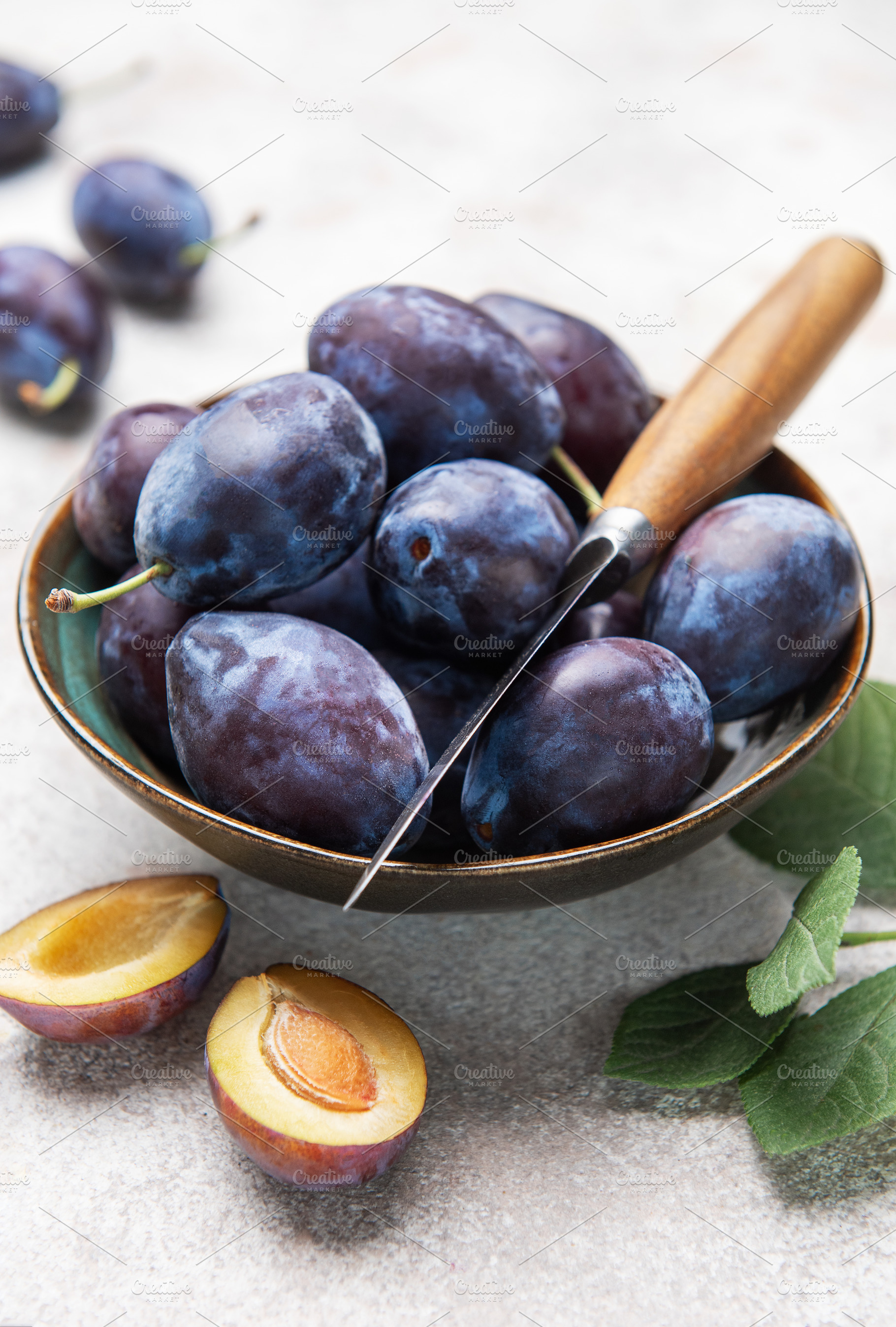 Fresh plums in bowl with knife on gray background, a Food & Drink Photo by Olena Rudo