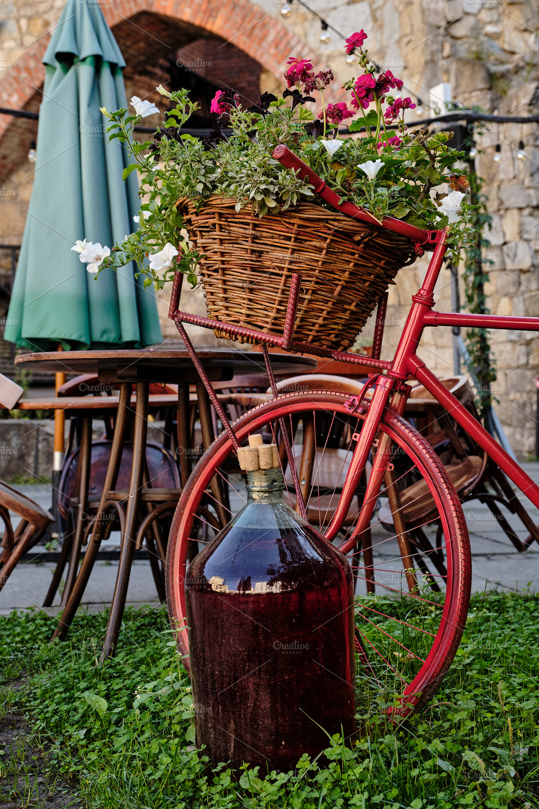 Red vintage bicycle with flower basket and large wine demijohn on a rustic cafe, a Nature Photo by Rohan Photography
