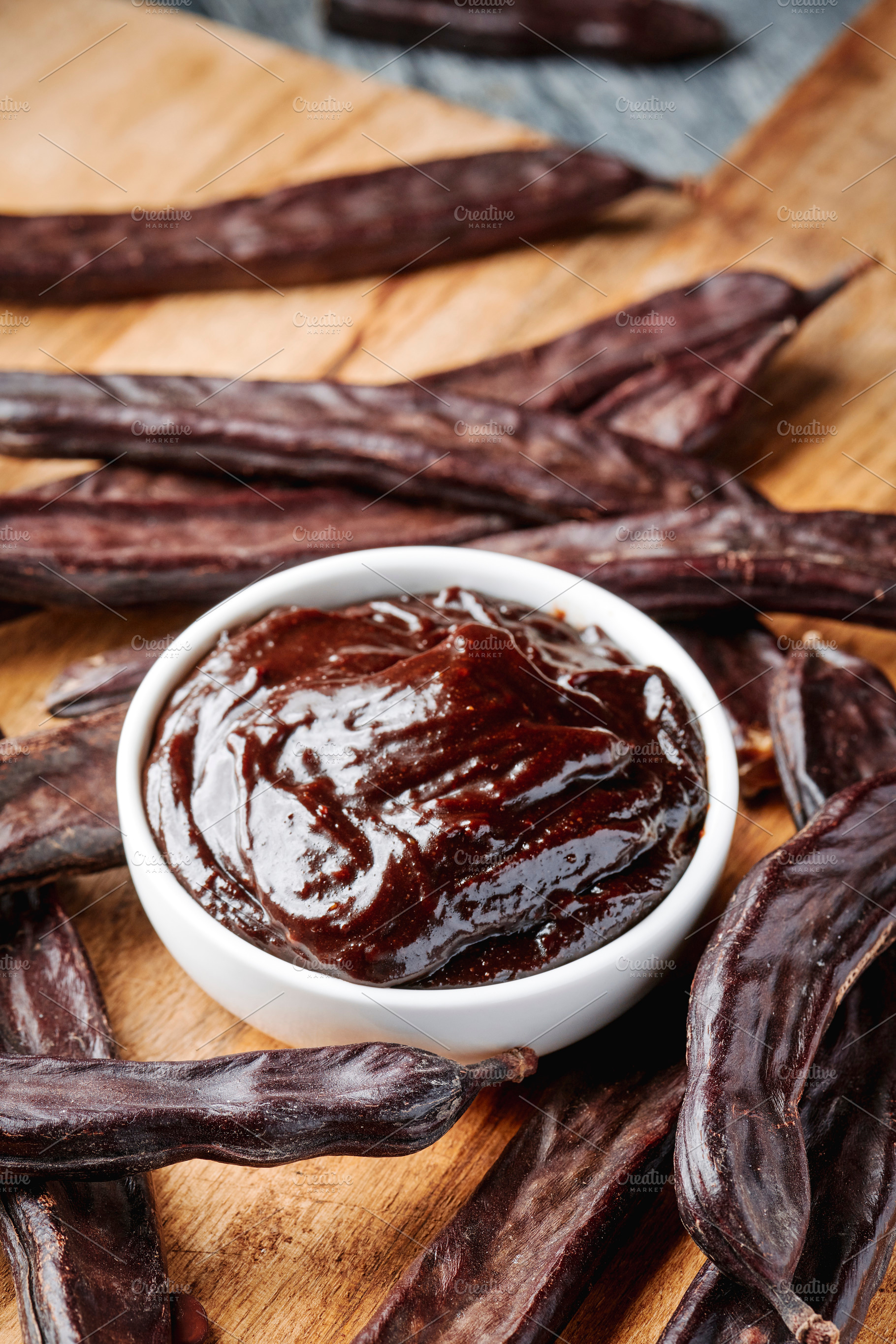bowl of carob spread and pods on a wooden table, a Photo by Nito