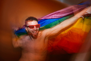 Man celebrating pride with rainbow flag and red sunglasses, a Photo by karrastock