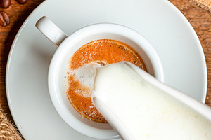 Barista pouring milk into a cup of coffee creating macchiato on wooden table wi, a Food & Drink Photo by Antonio Gravante Market