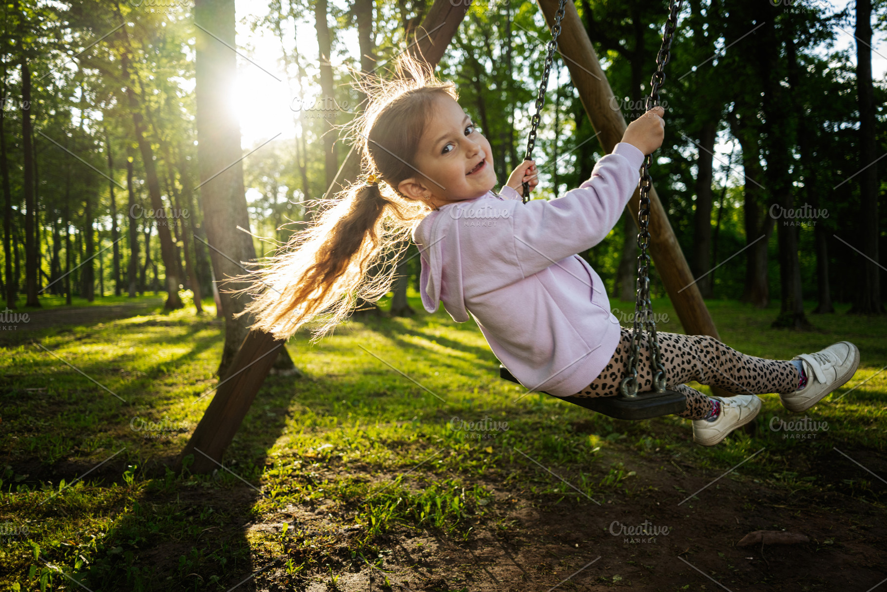 Young girl swinging in a green forest with evening sunlight, a Person Photo by AS photostudio